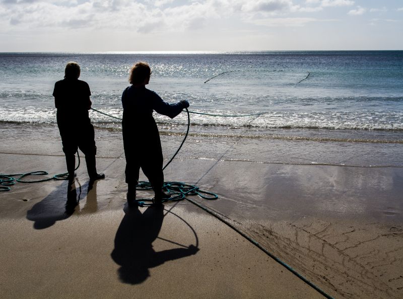 A pair of Cornish fisherman hauling their beach nets in as they fish for sand eels at Coverack in Cornwall.